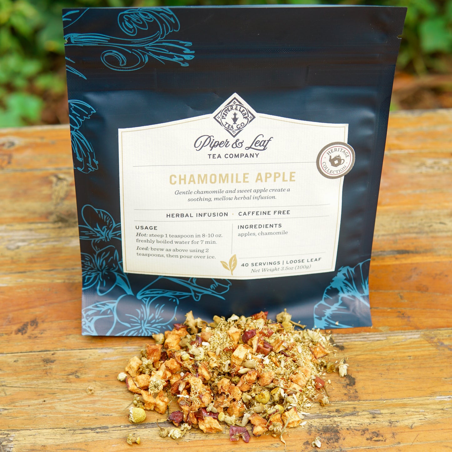 A package of Piper and Leaf Tea Co. Chamomile Apple 40 Serving Loose Leaf Tea rests on a wooden surface, with a small pile of the caffeine-free herbal blend displayed in front of it.