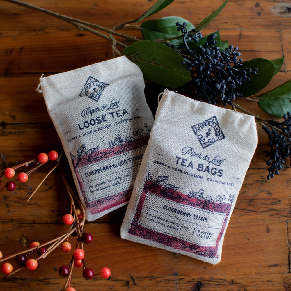 The Elderberry Elixir Muslin Bag of Loose Tea (15 servings) by Piper & Leaf Tea Co., pictured amid berries and green leaves, evokes the essence of an immune-boosting tonic.