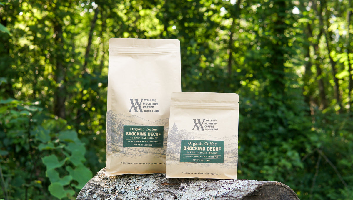 Two 3.5lb bags of Walling Mtn. Coffee's "Shockingly Tasty Decaf" sit on a tree stump with a forest background, highlighting the rich, medium-dark roast perfected in every small batch.