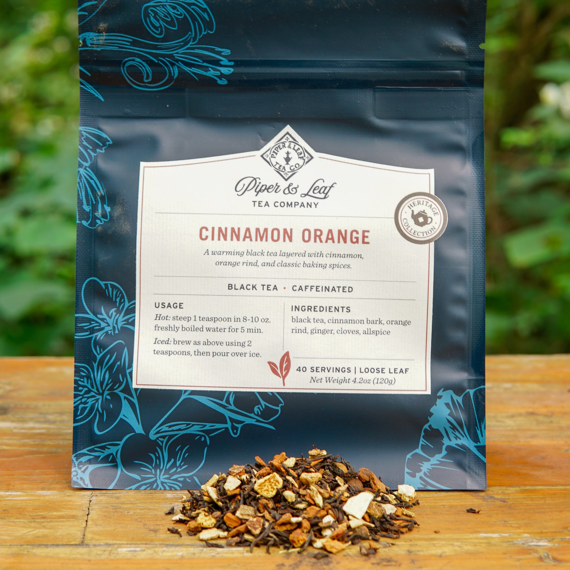 A package of Piper and Leaf Tea Co. Cinnamon Orange 40 Serving Loose Leaf Tea is displayed on a wooden surface, with a small pile of loose tea leaves and aromatic spices arranged in front.