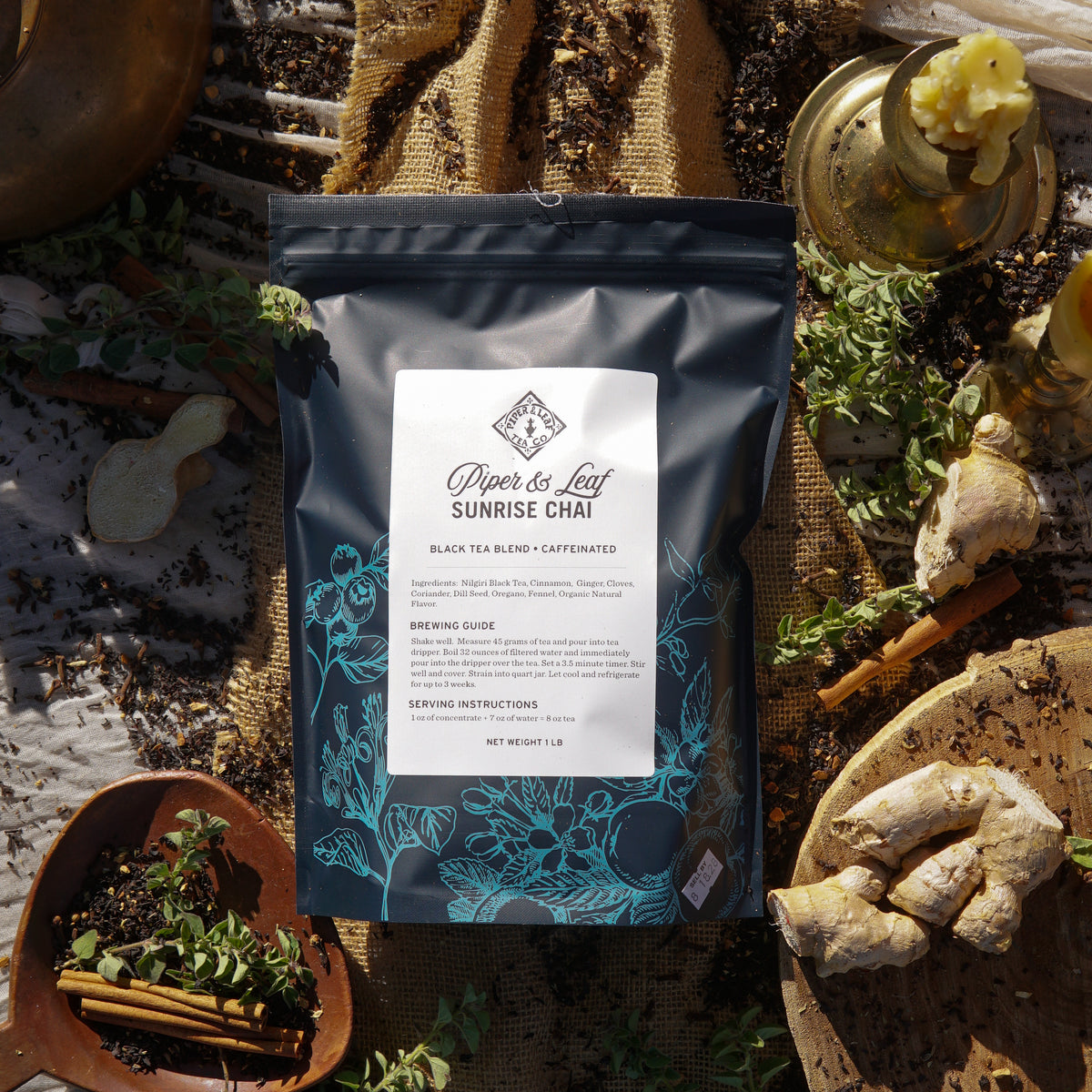 The Piper & Leaf Tea Co. Sunrise Chai Pound Bag (190 servings) is displayed with fresh ginger, tea leaves, and herbs on rustic cloth, bathed in warm sunlight.