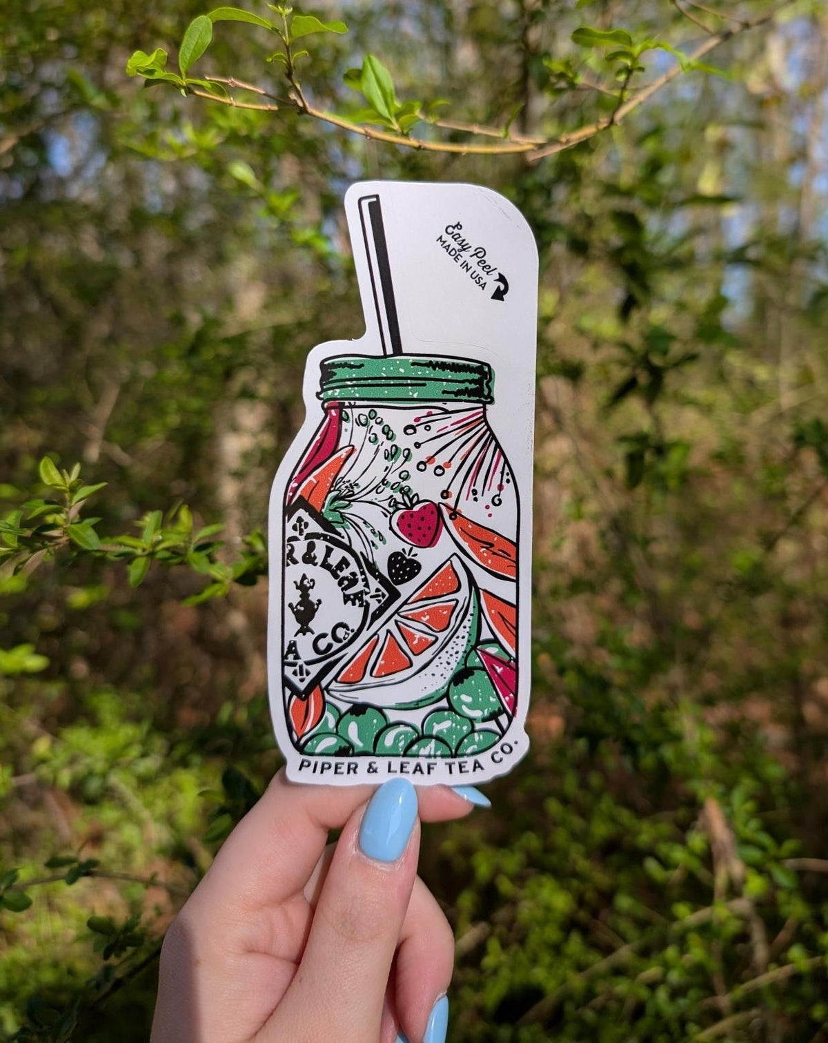A hand with light blue nail polish holds the Ninja Transfers Jar of Berries Sticker, shaped like a mason jar and surrounded by green foliage—ideal for spring or summer vibes.