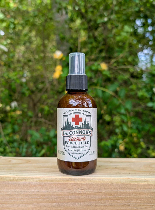 A brown bottle of Walling Mountain Farms' Dr. Connor's Ultimate Force Field Bug Spray for Clothing & Gear sits on a wooden surface with green foliage in the background.